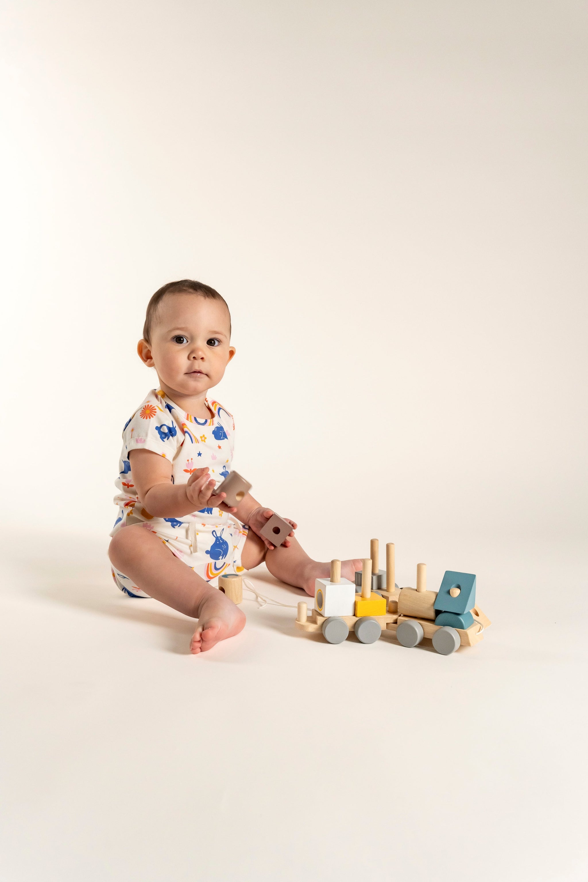 Toddler girl wearing a short sleeve t-shirt with a playful bunnies and rainbow print, featuring colorful suns, flowers, and stars. Made from soft organic cotton, perfect for casual wear and playtime.