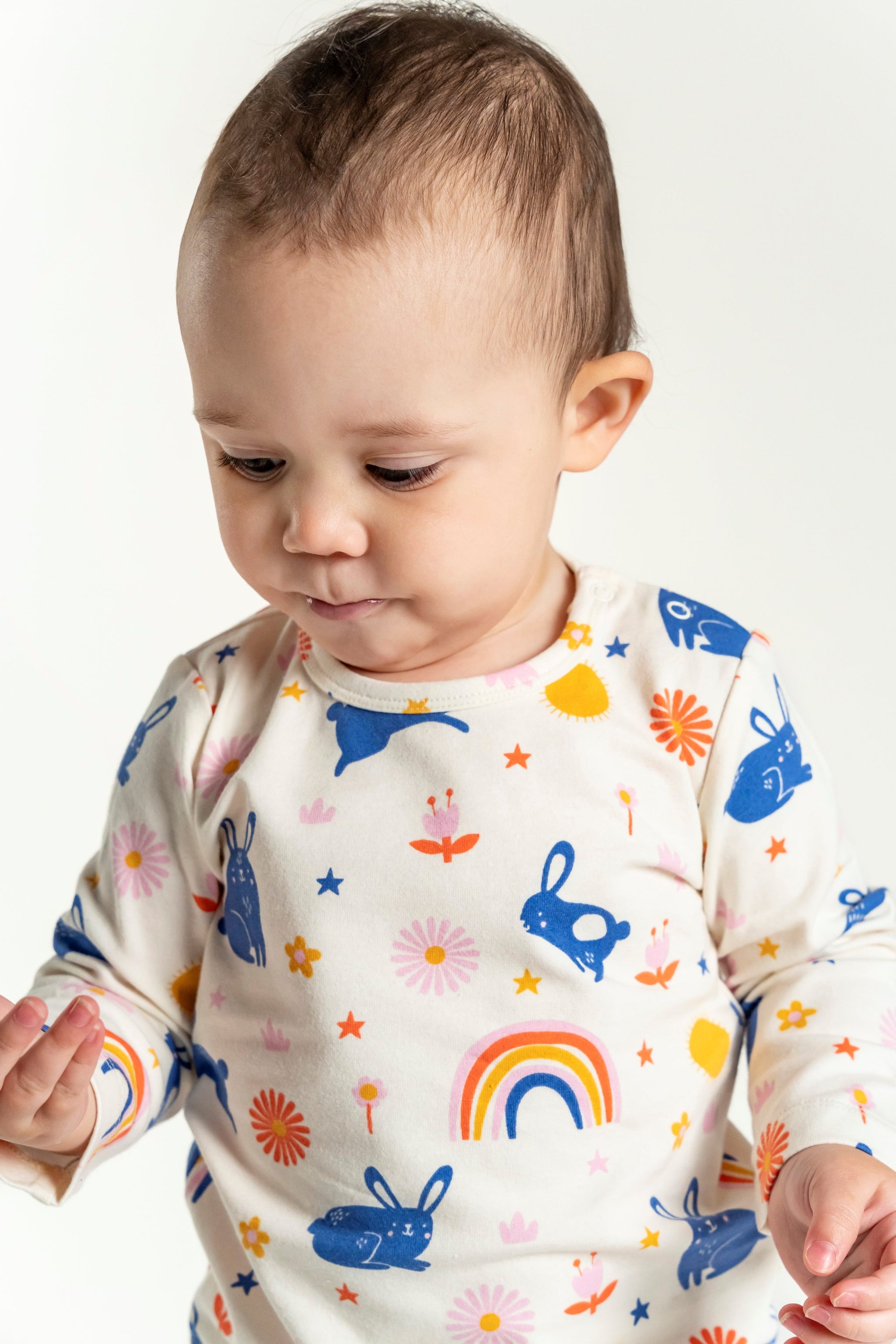 Toddler Girl Long Sleeve T-shirt with a playful Bunnies and Rainbow Print, featuring blue bunnies, colorful rainbows, stars, and flowers on a soft cream background. Ideal for everyday comfort and style.