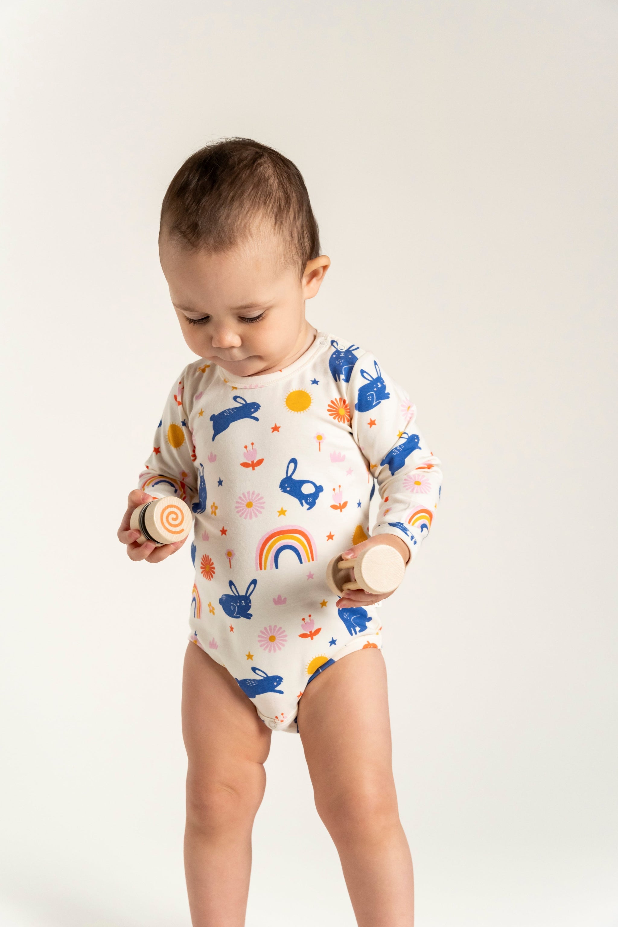 Toddler Girl Long Sleeve Bodysuit - Bunnies and Rainbow Print, featuring playful blue bunnies, vibrant rainbows, and floral designs. Soft cotton material perfect for everyday comfort and active play.