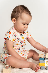 Toddler girl playing with wooden blocks while wearing a short sleeve t-shirt with a bright sunny flower print. Made from soft organic cotton, ideal for comfortable playtime and casual everyday wear.