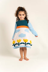 Toddler girl wearing Cloudy Daydream Cotton Knitted Sweater Dress with blue sleeves, cloud and yellow tulip patterns, and orange stripe. Cozy, long-sleeved cotton perfect for casual fall/winter outfits.