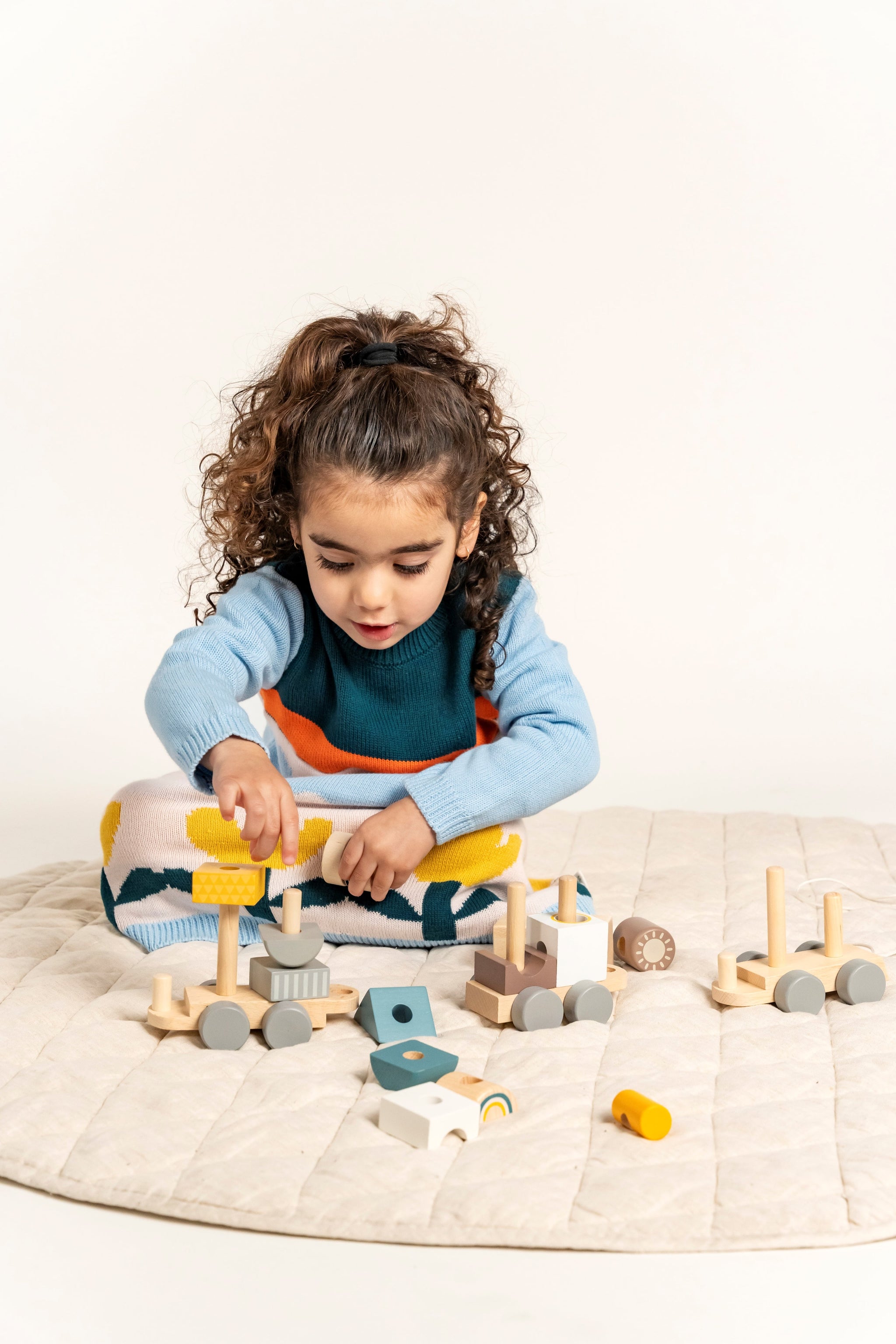 Toddler playing while wearing Cloudy Daydream Cotton Knitted Sweater Dress with blue sleeves, orange stripe, cloud patterns, and yellow tulips. Soft, cozy, long-sleeved dress perfect for fall/winter.