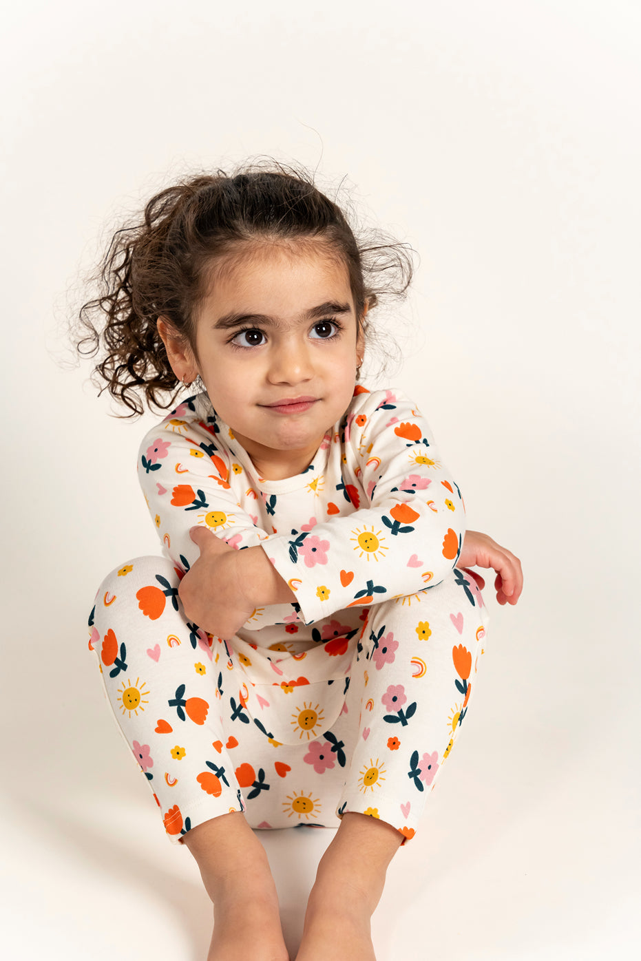 Cute toddler girl wearing a long sleeve T-shirt and slouchy pants set with a bright sunny flower print, sitting with a thoughtful expression, perfect for cozy and stylish everyday wear.