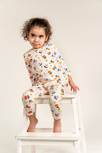 Adorable toddler girl wearing a long sleeve T-shirt and slouchy pants set with a bright sunny flower print, sitting playfully on a white step stool, perfect for a cozy and stylish everyday look.