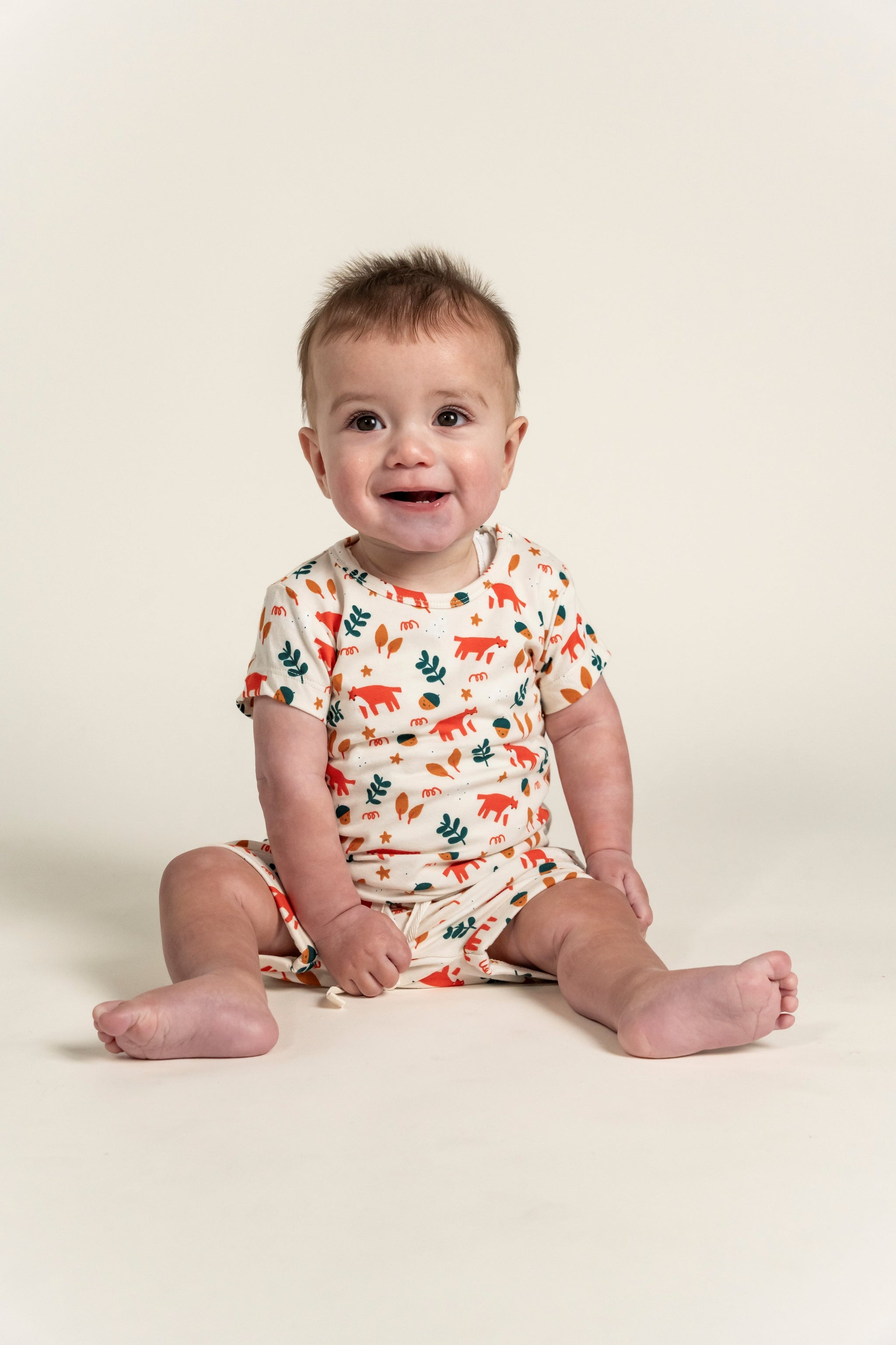 Smiling toddler boy in a short sleeve t-shirt with fox forest print, featuring playful red foxes and green leaves. Soft organic cotton, perfect for casual wear, playtime, and outdoor adventures.