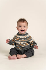 Baby wearing a cozy Fair Isle Sweater Jumper in dark grey with white and orange geometric patterns. Soft cotton, long-sleeved sweater perfect for keeping babies warm during fall and winter.