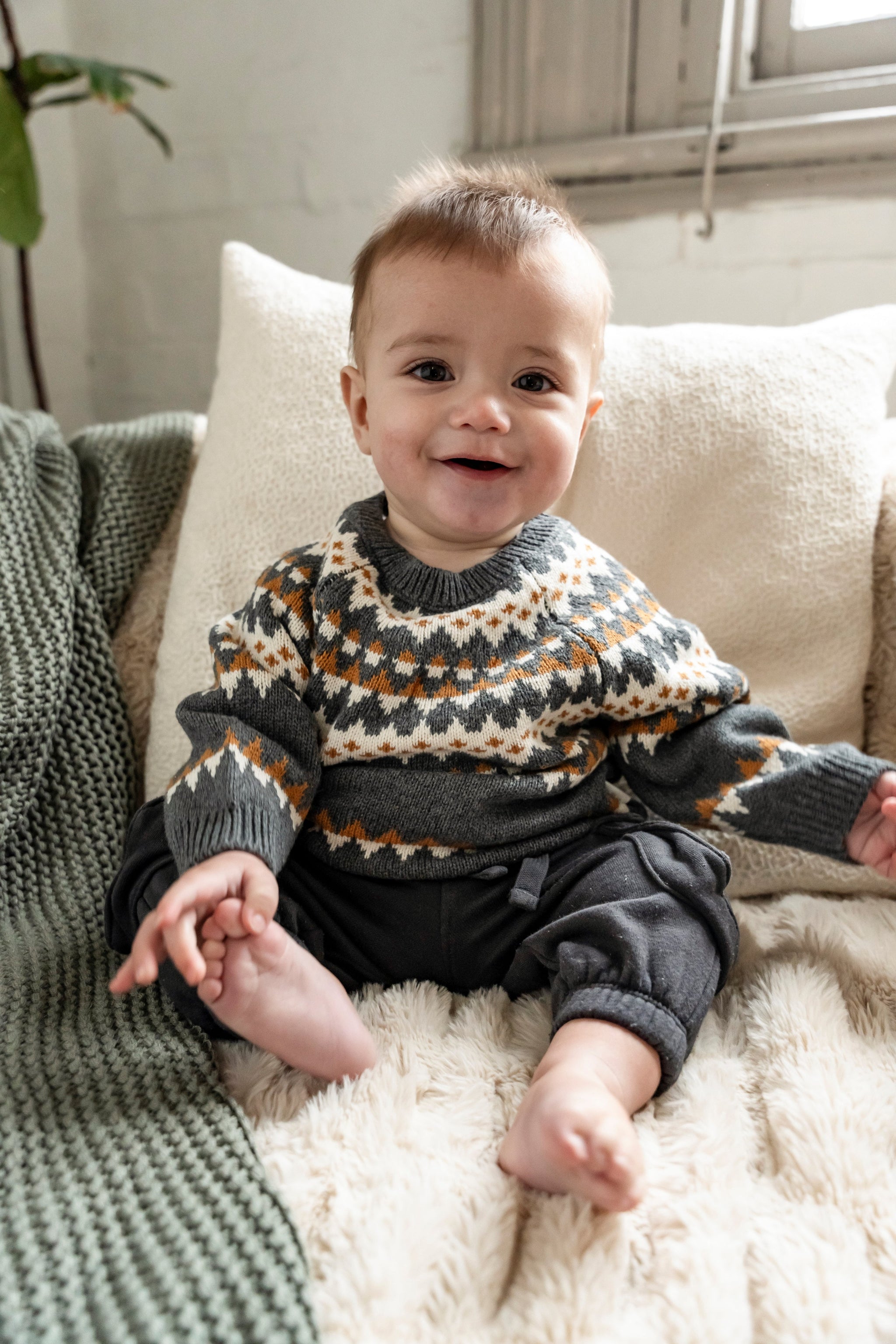 Baby wearing a cozy Fair Isle Sweater Jumper in dark grey with white and orange geometric patterns. Long-sleeved, soft cotton perfect for keeping toddlers warm during fall and winter. Ideal for casual wear.