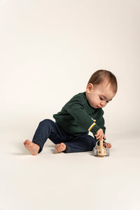 Charming baby playing with a wooden toy, wearing a forest green Waffle Cotton Knit Jumper featuring a stylish front pocket and yellow and white accents. Perfect for cozy, everyday wear and toddler fashion.