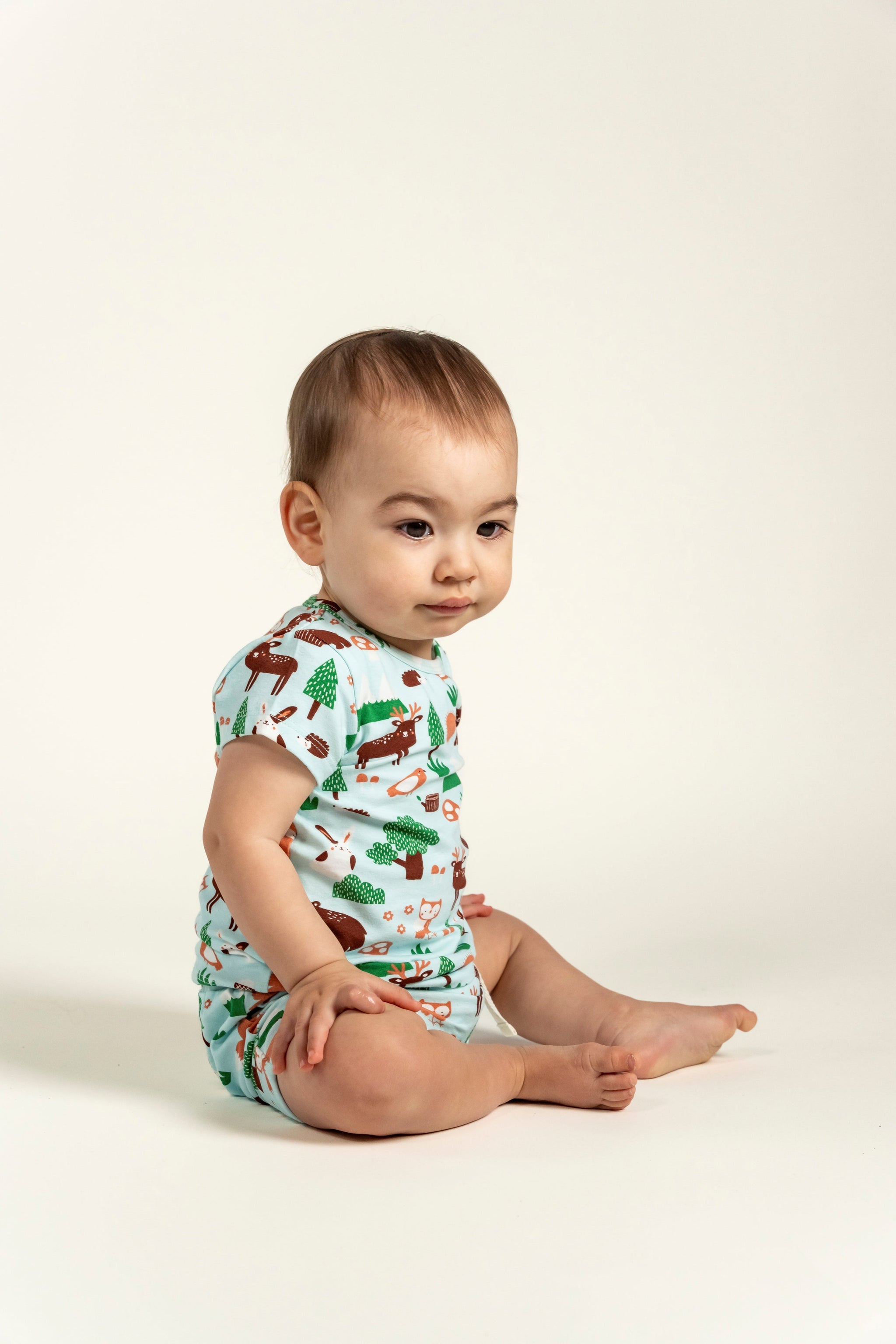 Cute toddler boy wearing a short sleeve t-shirt with forest animal print featuring deer, rabbits, and trees. The lightweight and breathable fabric is perfect for outdoor play and everyday wear.