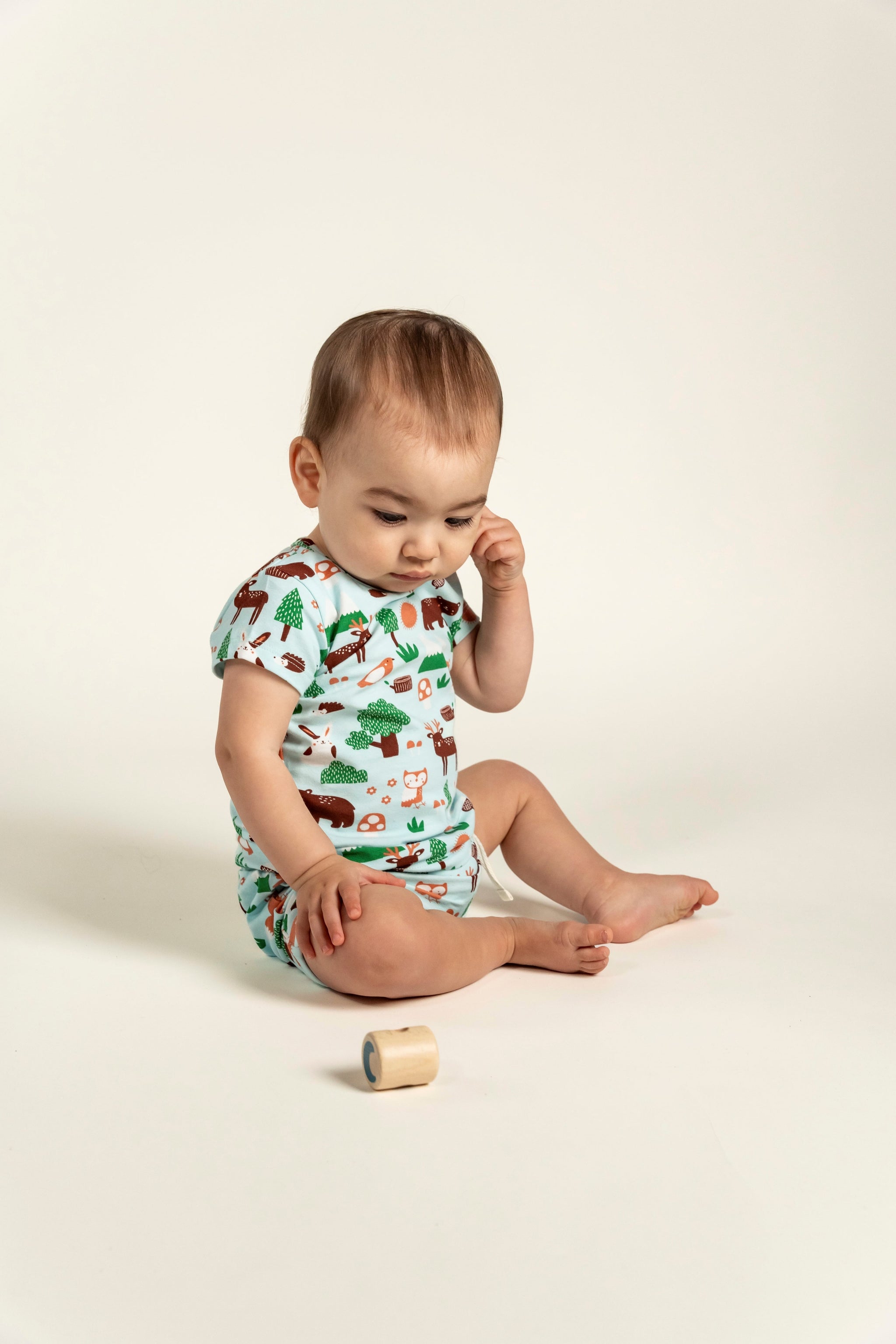 Toddler boy in a short sleeve t-shirt with forest animal print, playing with a wooden block. Featuring bears, trees, and foxes, this soft, breathable tee is ideal for active, everyday play.