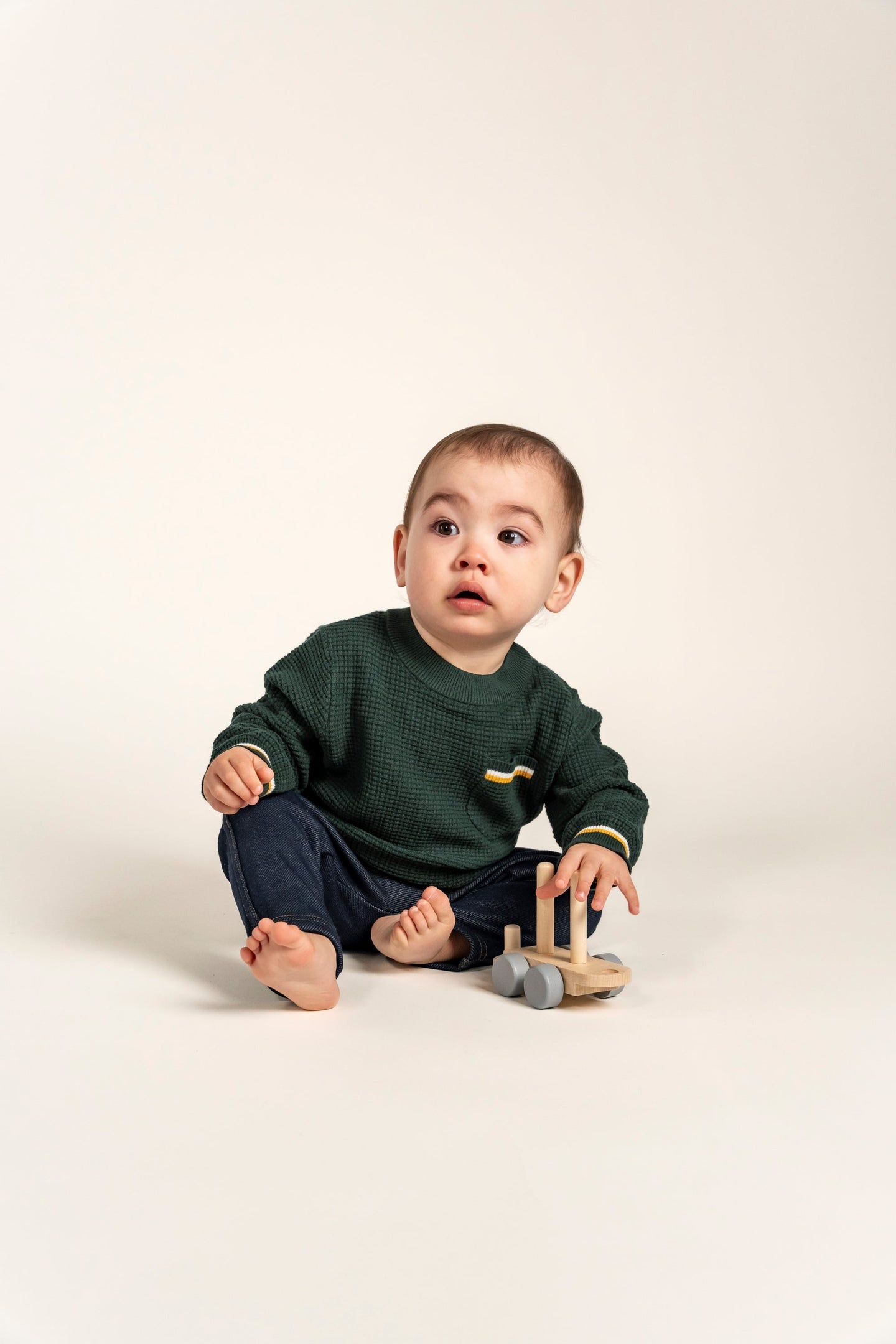 Adorable baby wearing a forest green Waffle Cotton Knit Jumper with yellow and white striped accents on the pocket, cuffs, and hem. Perfect for cozy warmth and style, ideal for everyday wear and playtime.