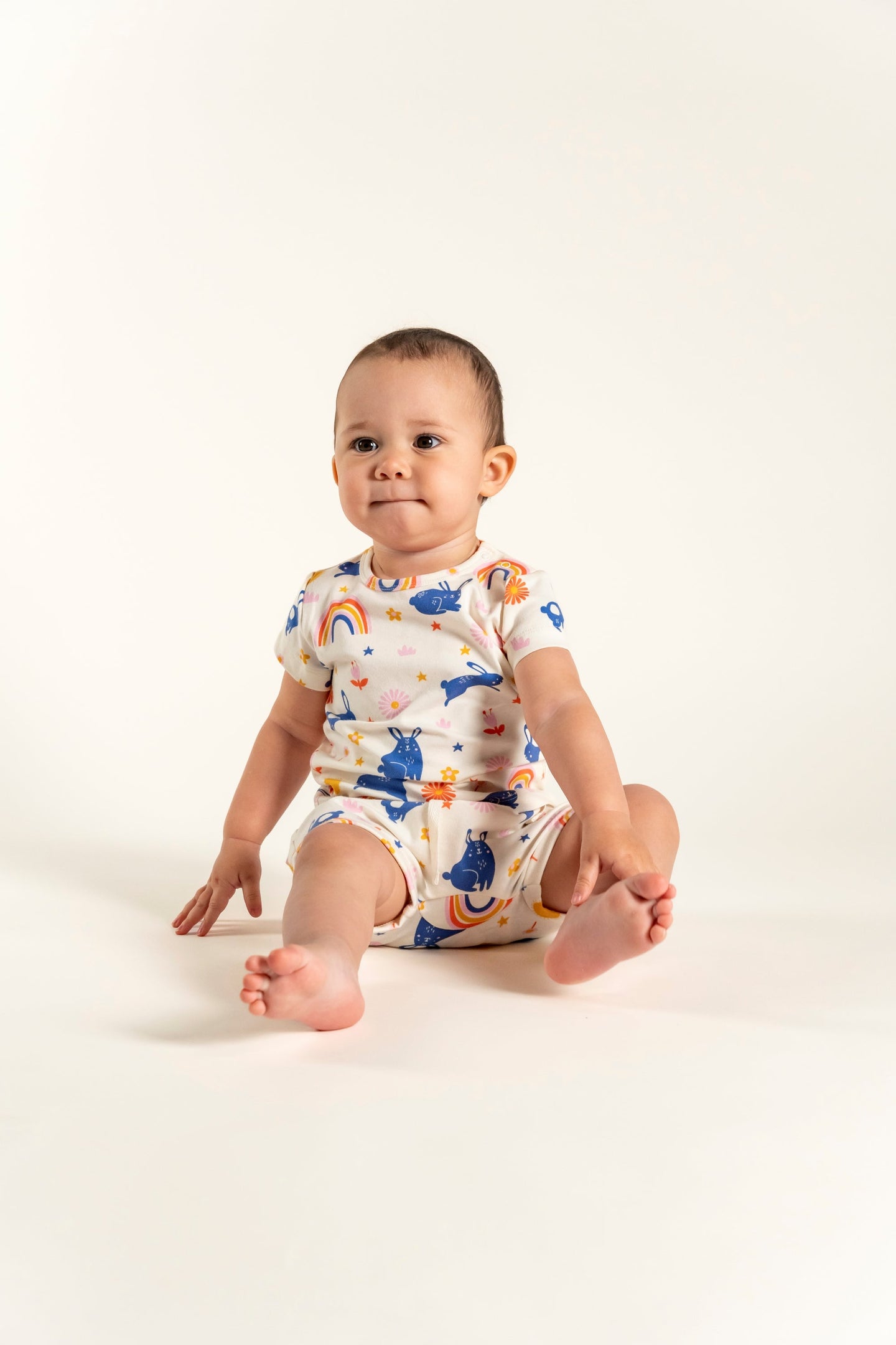 Adorable toddler girl wearing a short sleeve t-shirt with bunnies and rainbow print, featuring colorful flowers and stars. Made from soft organic cotton, perfect for casual wear, playtime, and outdoor fun.