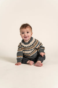 Baby wearing a Fair Isle Sweater Jumper in dark grey with white and orange geometric patterns. Cozy, long-sleeved, soft cotton ideal for keeping toddlers warm during fall and winter. Perfect for casual outfits.