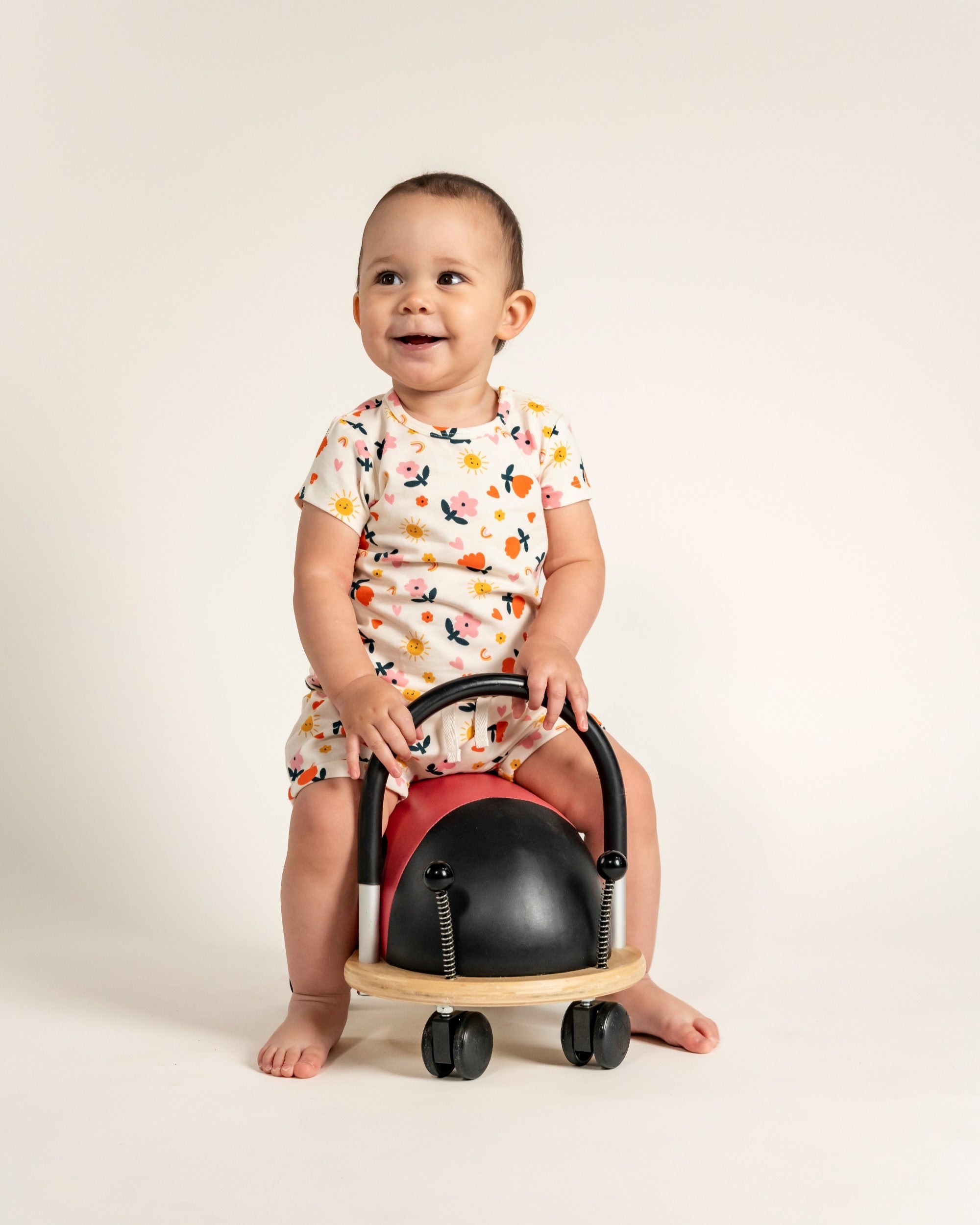 Toddler girl wearing short sleeve t-shirt and slouchy shorts set with Sunny Flower print, featuring colorful sun, flowers, and leaf patterns on a cream background. Comfortable, playful outfit for toddlers.